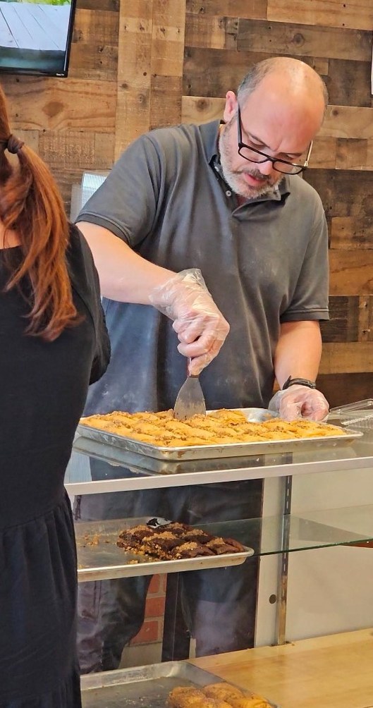 Rami Wadee at the counter cutting baklava at Al-Taj Mediterranean Bakery & Sweets in Lexington